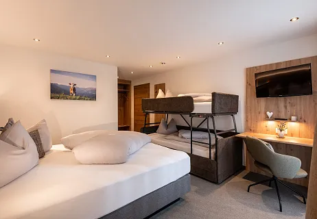 Modern eingerichtetes Hotelzimmer mit Doppelbett, Etagenbett und Schreibtisch in den Alpen.