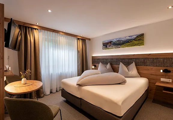 Hotelzimmer in Tirol mit Doppelbett, Vorhängen und Landschaftsfoto an der Wand.