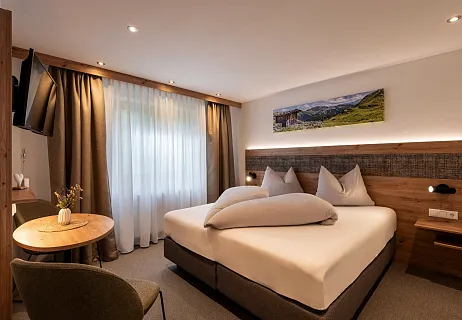 Hotelzimmer in Tirol mit Doppelbett, Vorhängen und Landschaftsfoto an der Wand.