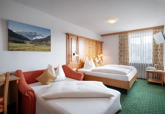 Hotelkamer met twee bedden, houten meubels en een schilderij van de Alpen aan de muur.