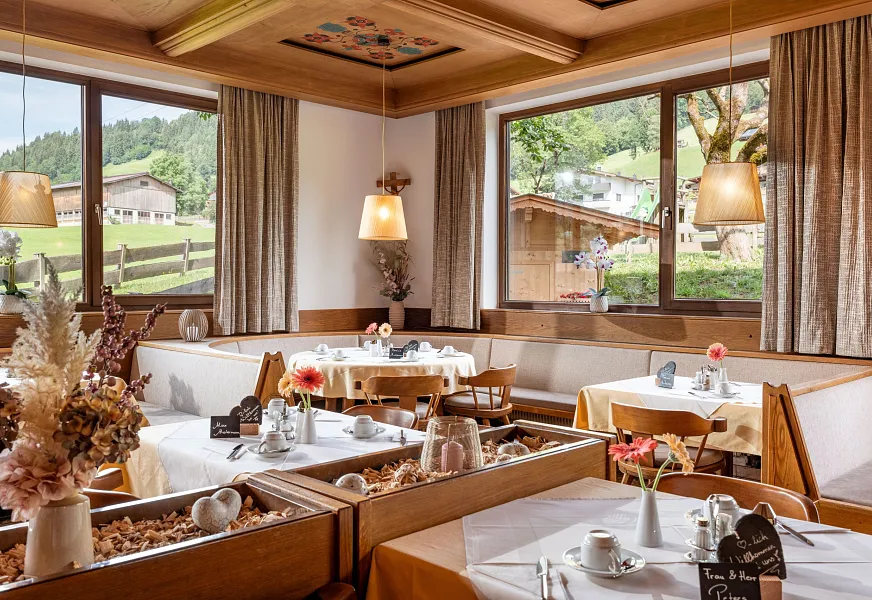 Gemütliches Restaurant mit Holztischen und großen Fenstern mit Blick auf eine alpine Landschaft.