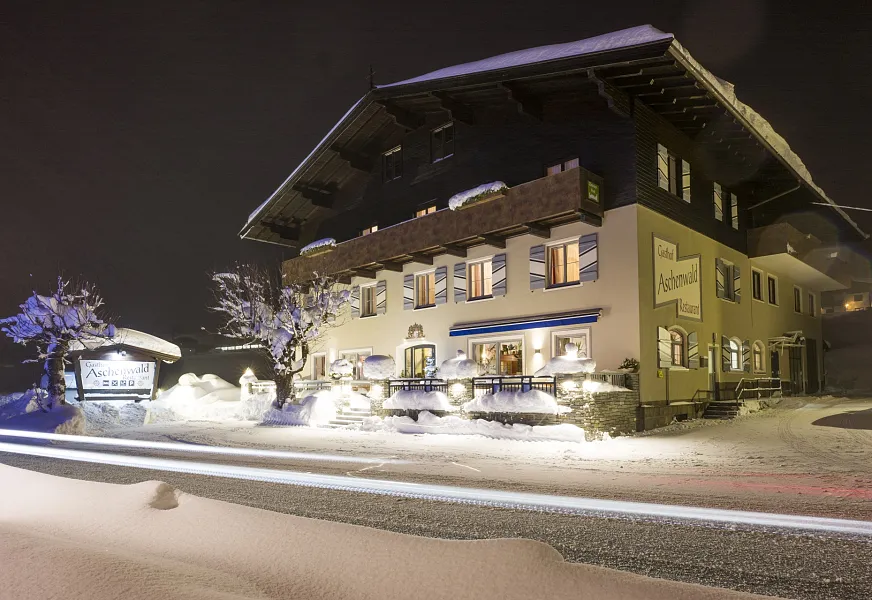 Ein verschneites Gebäude in Tirol bei Nacht, beleuchtet mit glänzendem Schnee auf dem Dach und Umgebung.