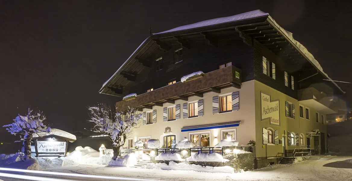 Ein verschneites Gebäude in Tirol bei Nacht, beleuchtet mit glänzendem Schnee auf dem Dach und Umgebung.