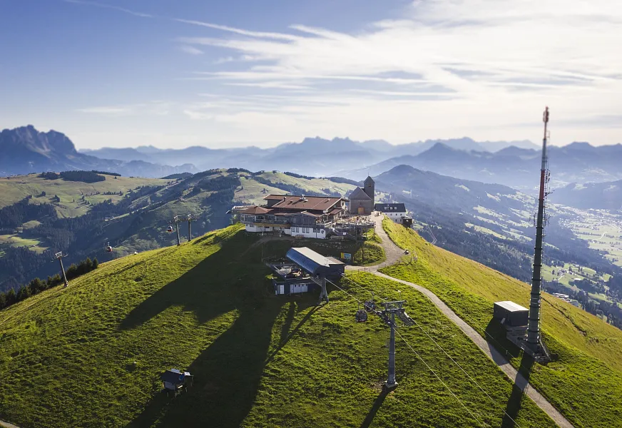 Mountain landscape in Kitzbühel with a building and antenna on the summit, surrounded by the Alps.