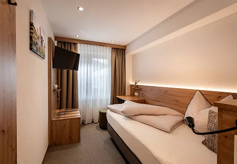 Gezellig ingerichte hotelkamer met een eenpersoonsbed, houten meubels en een flatscreen-tv aan de muur.