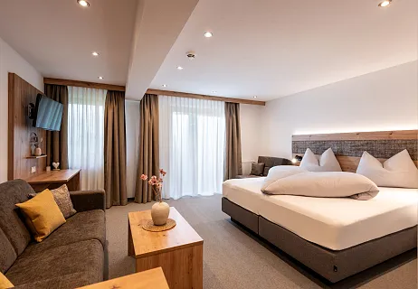 Modernes Hotelzimmer mit Doppelbett, Sofa und Tisch, neutral dekoriert.