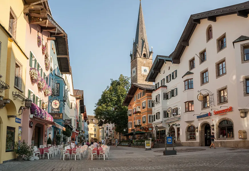 Malerische Altstadt von Kitzbühel mit bunten Gebäuden und einem Kirchturm bei klarem Himmel.