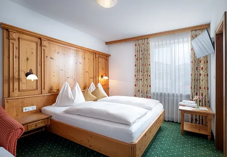 Knus hotelkamer met traditioneel houten meubilair en een groen tapijt, met een groot bed en een raam met uitzicht.