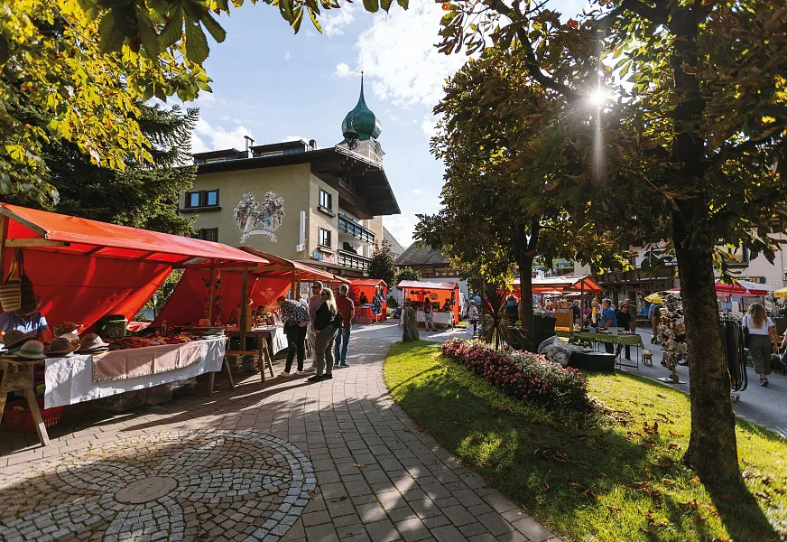Decorated cows parade through a street during a festival in Tirol, with people watching in the background.
