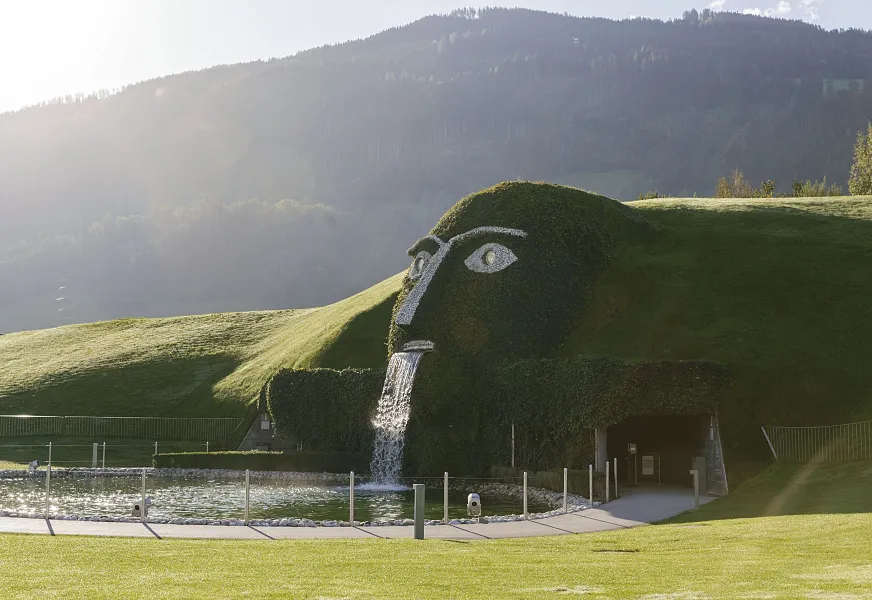 Grüne Landschaft mit einer Skulptur eines Gesichts aus Gras und Wasserfall bei den Swarovski Kristallwelten in Tirol.