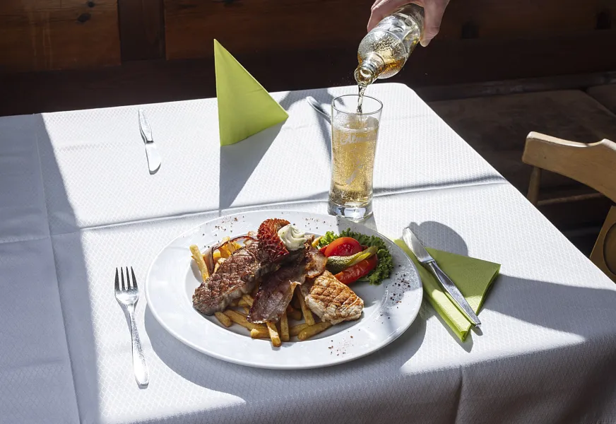 Ein Teller mit Fleisch, Pommes frites und Gemüse auf einem Tisch mit einem Getränk, das daneben eingeschenkt wird.
