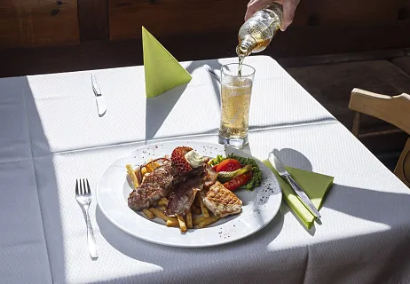Ein Teller mit Fleisch, Pommes frites und Gemüse auf einem Tisch mit einem Getränk, das daneben eingeschenkt wird.