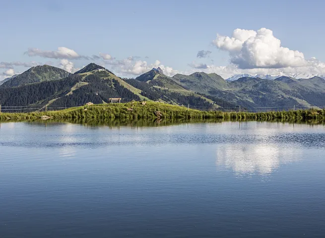 Alpenlandschaft mit See in Kitzbühel, Tirol, umgeben von grünen Bergen und blauem Himmel.