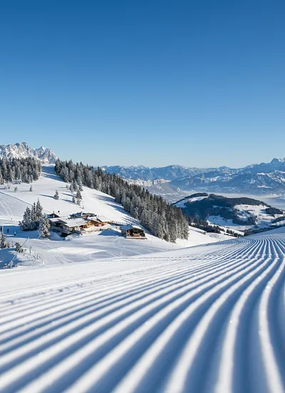 Verschneite Alpenlandschaft in Tirol mit präparierter Piste und Hütten im Hintergrund.